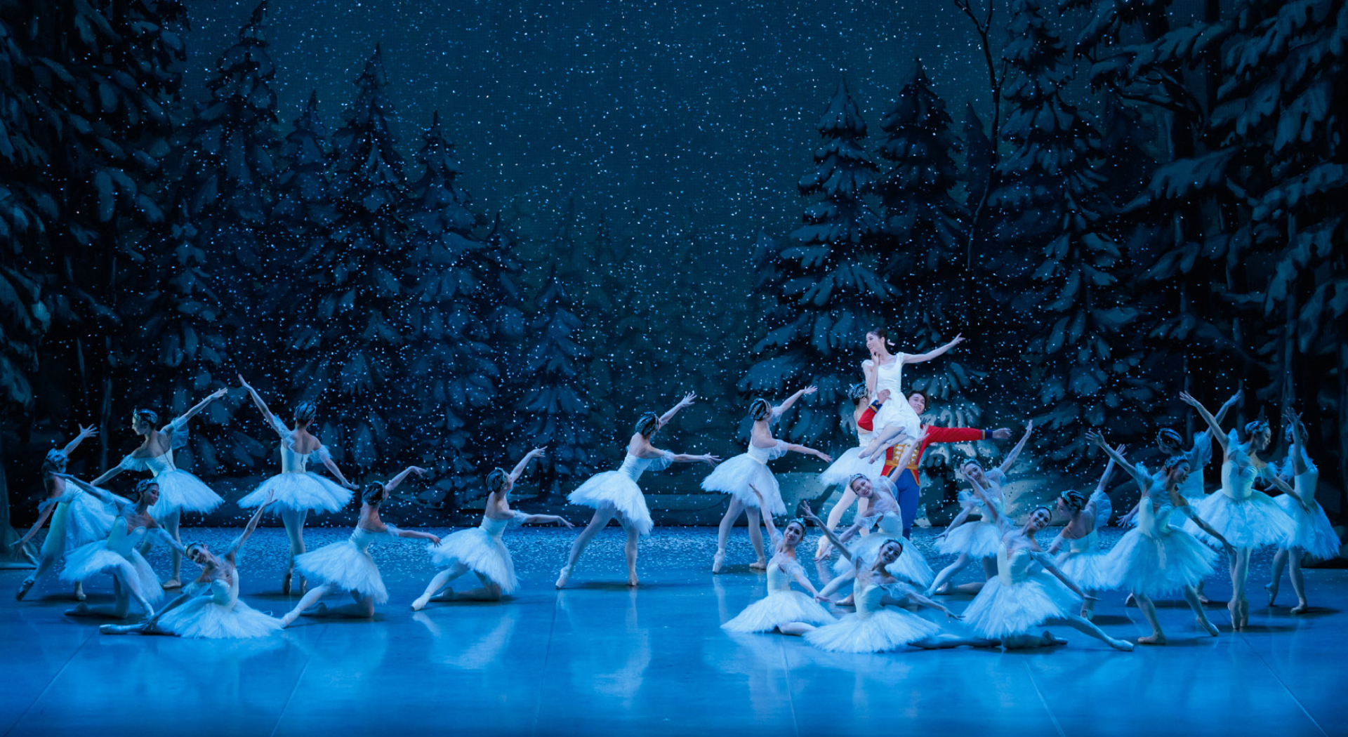 舞台の上で白い衣装のバレエダンサーたちが雪景色のセットの中で踊っている